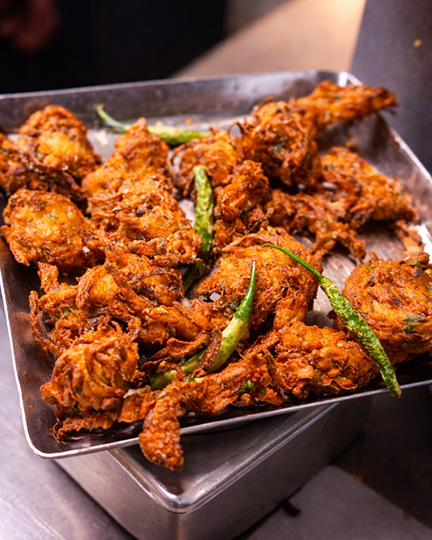 Freshly fried onion bhaji pakoras with green chillies on a steel serving tray